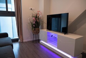 A modern living room with a flat-screen TV on a white console, a potted plant, and a sofa.