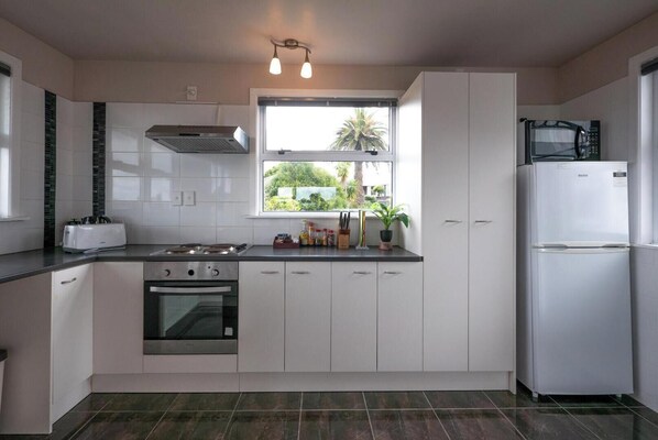 Une cuisine moderne avec des meubles blancs, une cuisinière à gaz, un four, un four à micro-ondes et un réfrigérateur. Une fenêtre offre une vue sur la verdure environnante.