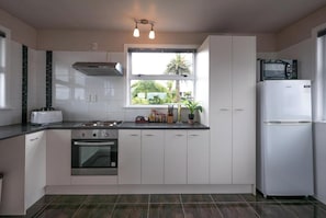 A modern kitchen with white cabinets, a gas stove, an oven, a microwave, and a refrigerator. There is a window with a view of greenery outside.