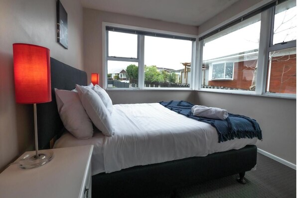 Een hotelkamer met een bed, nachtkastje, lamp en grote ramen met uitzicht.