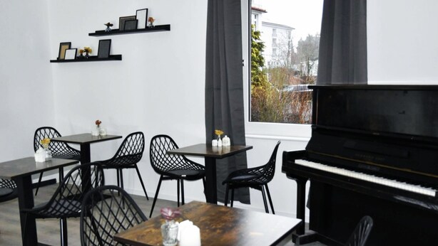 Un comedor con un piano, sillas negras y mesas.