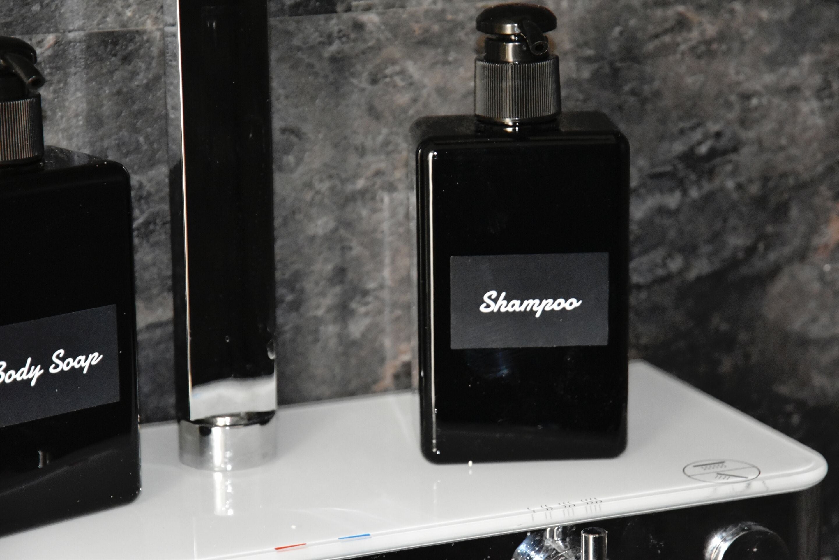 Duas garrafas pretas de shampoo e sabonete líquido sobre uma bancada branca.