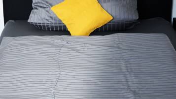 A bed with a striped gray bedspread, a black headboard, and a single yellow pillow.