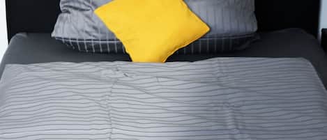 A bed with a striped gray bedspread, a black headboard, and a single yellow pillow.