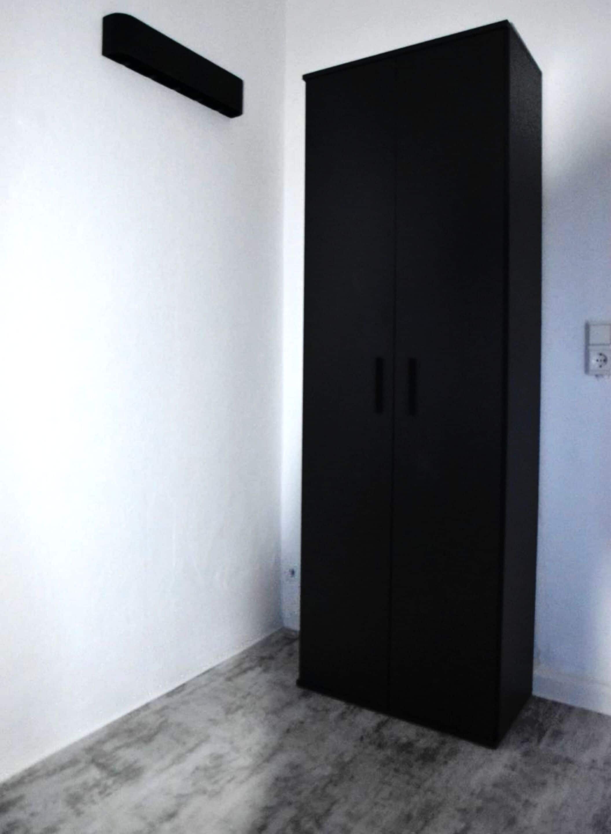 A room with a black wardrobe, a marble floor, and a white wall.
