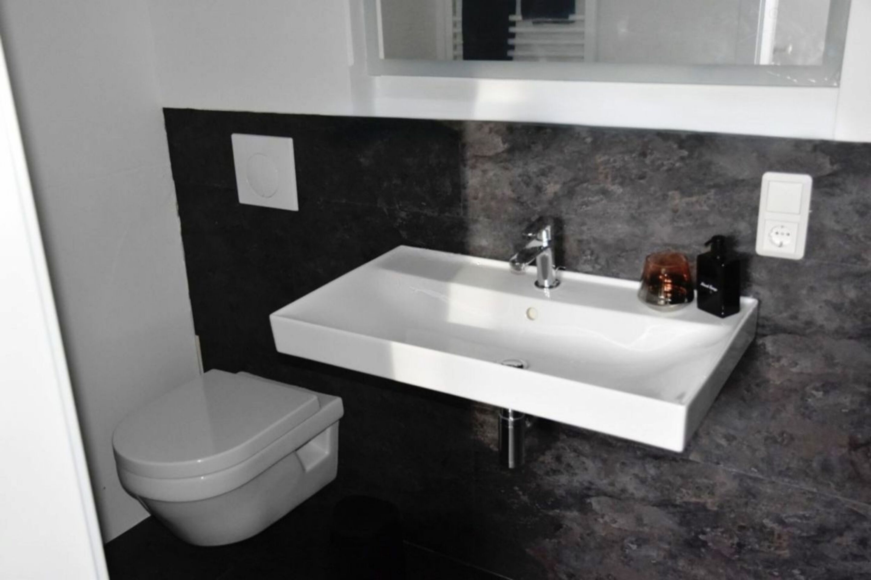 Un baño con lavamanos blanco, encimera negra y retrete blanco.