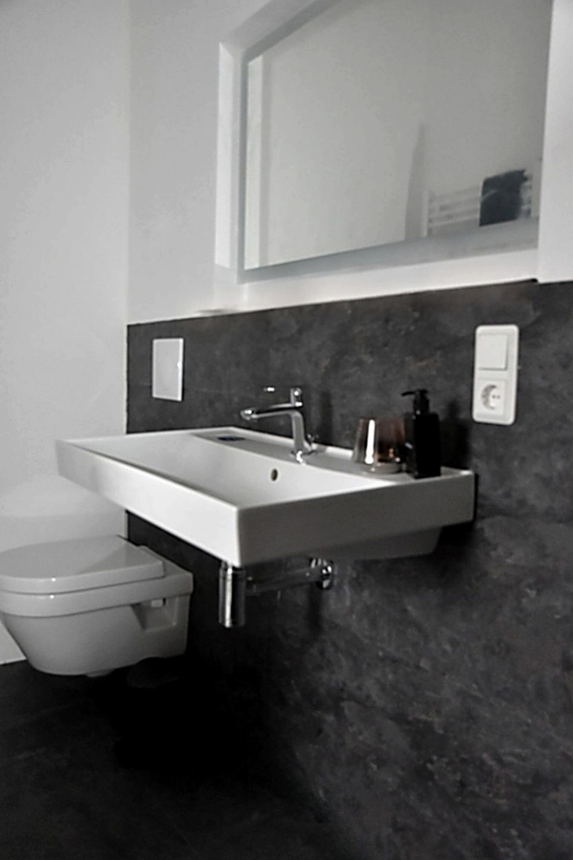 Ein modernes Badezimmer mit einem weißen Waschbecken, einer dunklen Arbeitsplatte und einer Toilette.