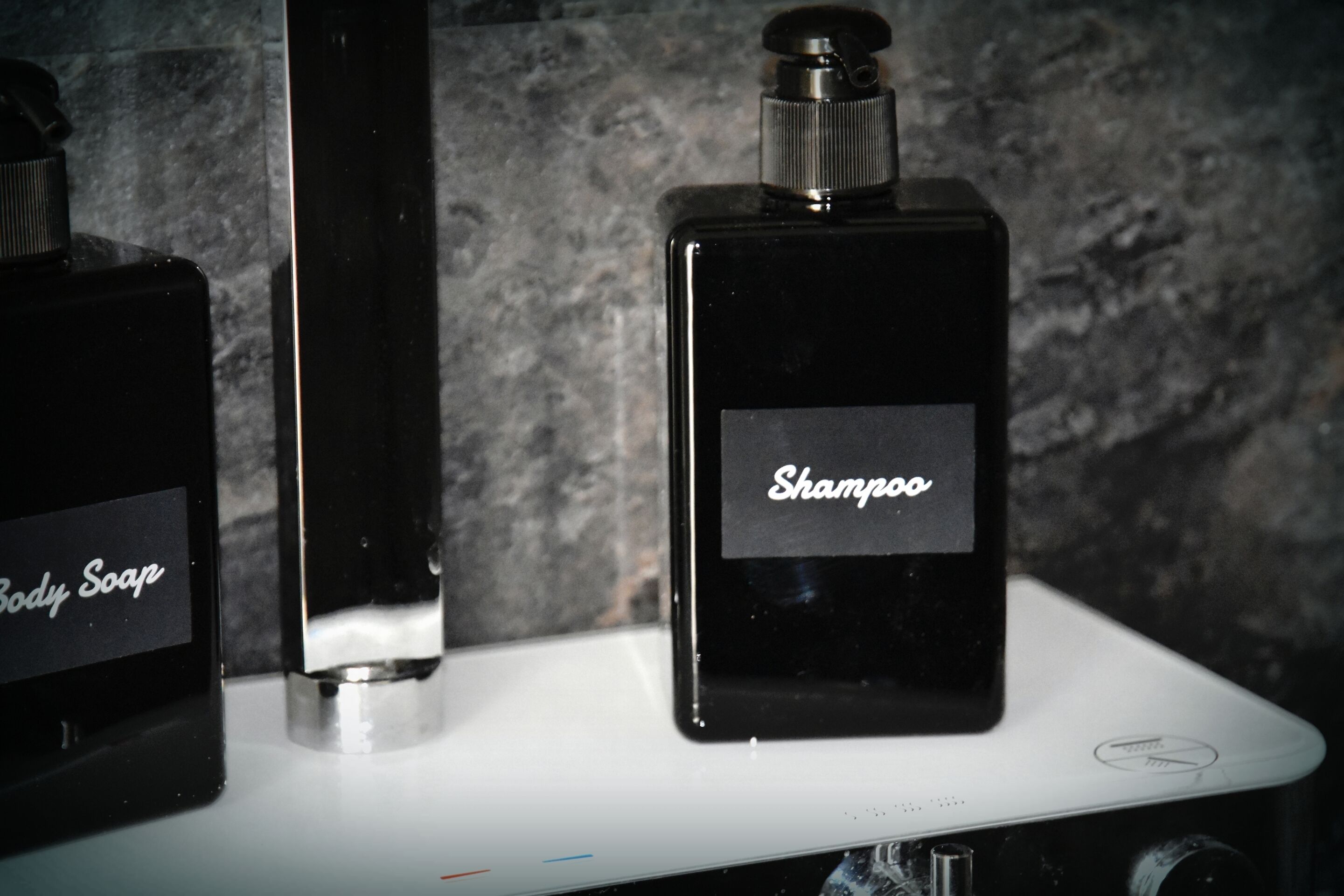 Two bottles of shampoo and body soap on a white surface against a textured background.