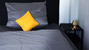 A bed with striped bedding, a single yellow pillow, and a black headboard.
