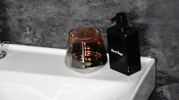 A bathroom sink with a glass container and a black bottle.