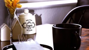 Una mesa de comedor con un dispensador de azúcar, un jarrón con flores amarillas, una taza negra y una servilleta.