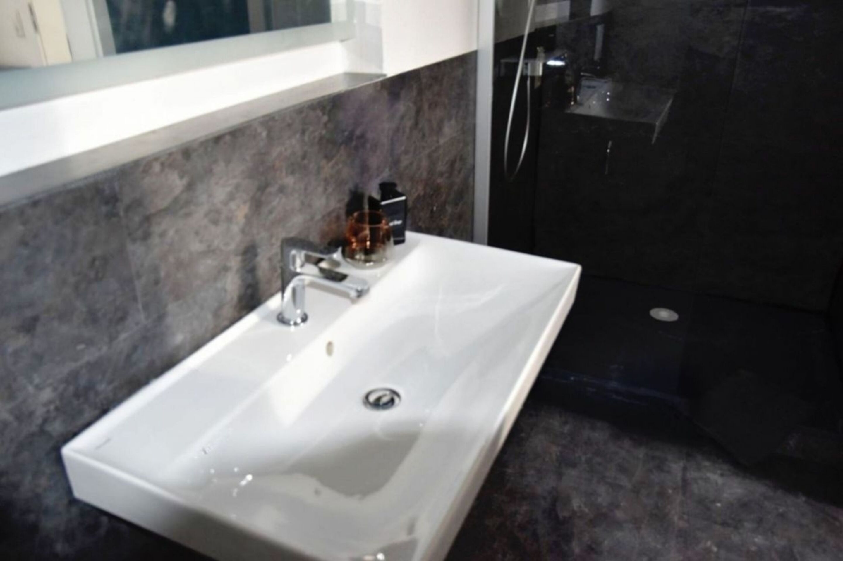 Ein modernes Badezimmer mit einem weißen Waschbecken, dunklen Marmorwänden und einer Glasdusche.
