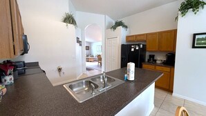A kitchen with granite countertops, stainless steel sink, wooden cabinets, and a refrigerator.