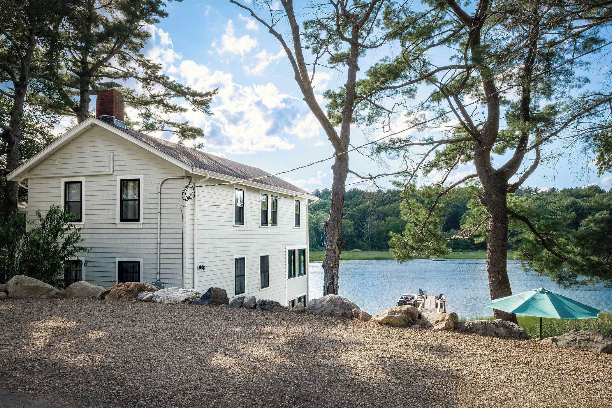 Une maison à deux étages avec une cheminée, une allée en gravier et une vue sur le lac.