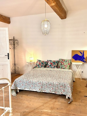 A bedroom with a floral bedspread, a hanging light fixture, and a painting on the wall.