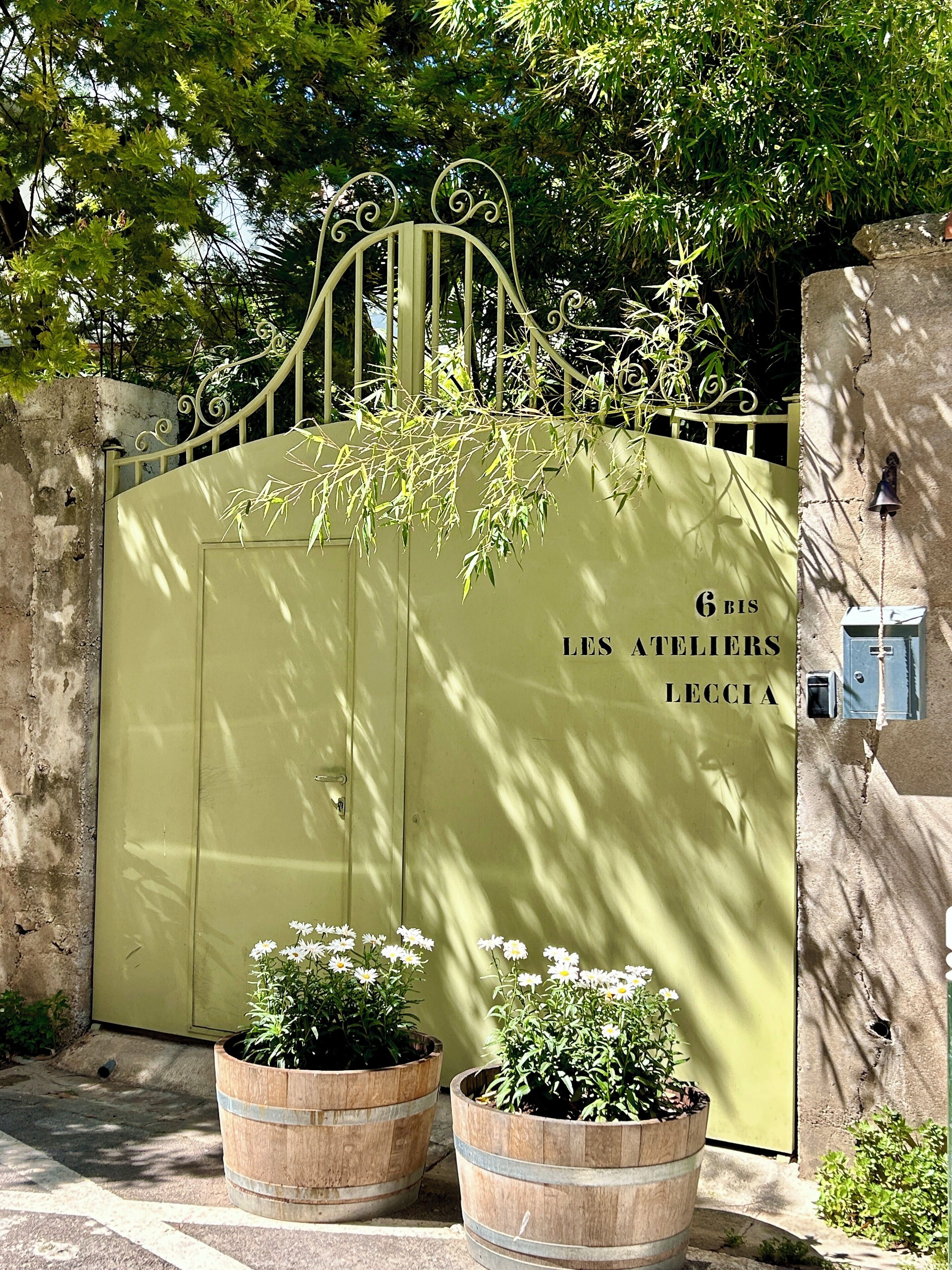 A gated entrance with a metal gate and a sign reading "6 BIS LES ATELIERS LECCIA".