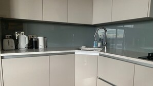 A modern kitchen with white cabinets, a stainless steel sink, and a countertop with a kettle, coffee maker, and a bottle of water. - 2 Bed Flat - Sleeps 4 - Parking - Wifi (London)