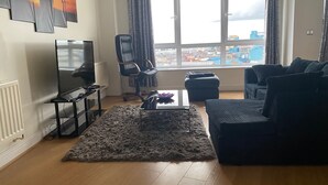 A living room with a large window, a flat-screen TV, a black leather chair, a black sofa, and a patterned rug. - 2 Bed Flat - Sleeps 4 - Parking - Wifi (London)