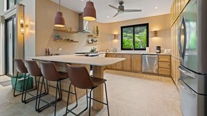 A modern kitchen with a central island, bar stools, pendant lighting, a ceiling fan, and a large refrigerator. - Private 4BR Oasis + Pool – Near Playa Grande Beach (Playa Grande)