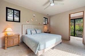 Une chambre à coucher comprenant un lit, une table de chevet, une lampe, un ventilateur de plafond et une vue sur l’extérieur.
