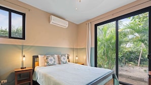 A bedroom with a bed, bedside lamps, an air conditioner, and a large sliding glass door leading to a garden. - Private 4BR Oasis + Pool – Near Playa Grande Beach (Playa Grande)