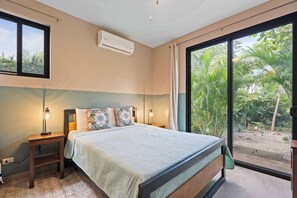 Ein Schlafzimmer mit Bett, Nachttischlampen, einer Klimaanlage und einer großen Schiebeglasdoor, die in einen Garten führt.