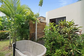 Une baignoire en béton dans un jardin luxuriant, avec un bâtiment moderne en arrière-plan.