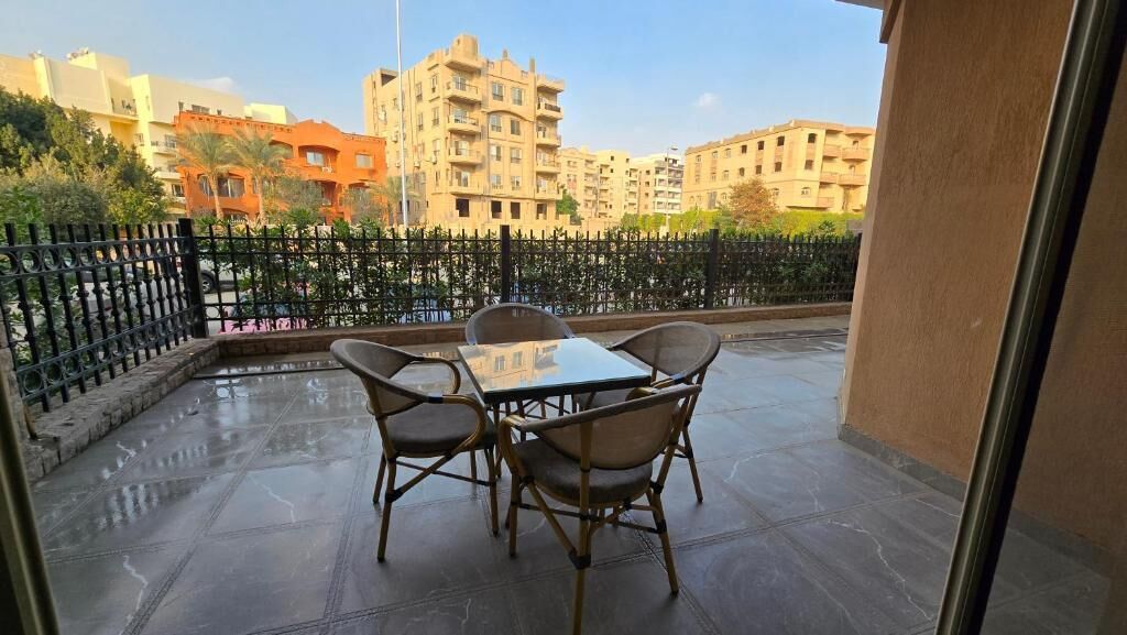 Un balcon avec une table et des chaises, une clôture en métal noir et des bâtiments en arrière-plan.