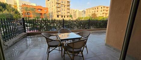 Un balcon avec une table et des chaises, une clôture en métal noir et des bâtiments en arrière-plan.