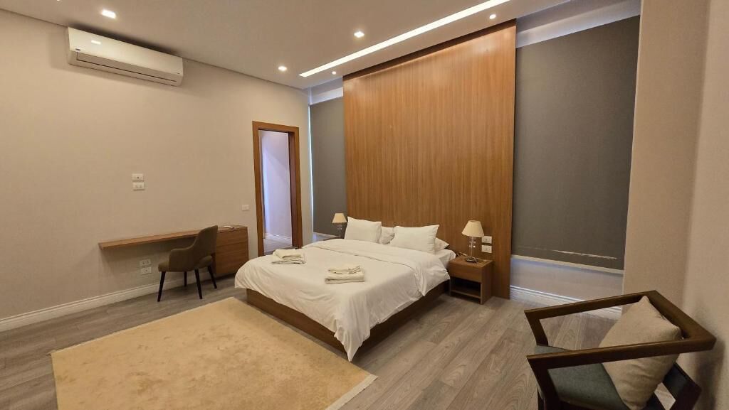 A modern bedroom with a large bed, bedside tables, a desk, and a chair.
