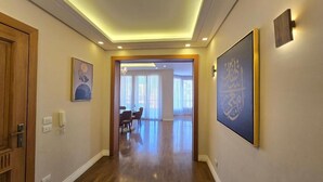 A hallway with wooden flooring, a door on the left, and a framed artwork on the right. - Maison 7 New Cairo  (New Cairo)