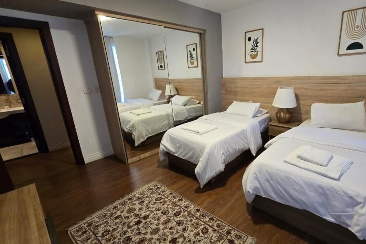 A hotel room with two beds, a mirror, a nightstand, a lamp, and a rug.