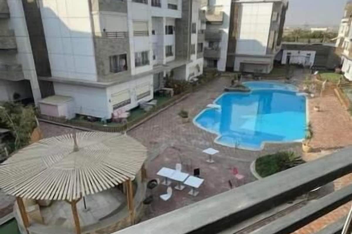 Un immeuble résidentiel doté d’une piscine, d’un espace salon couvert et offrant une vue sur le quartier environnant.