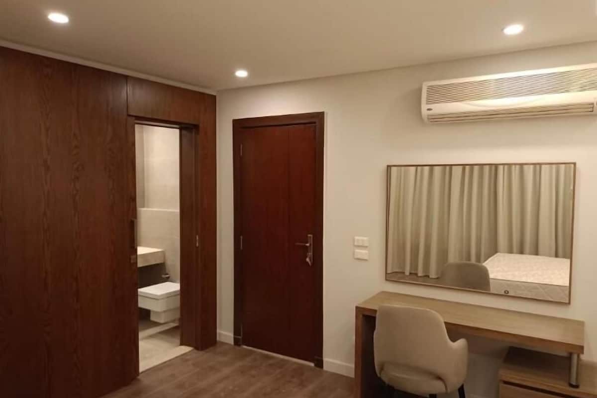 Une chambre avec une armoire en bois, un bureau avec une chaise, un grand miroir et un système de climatisation intégré.