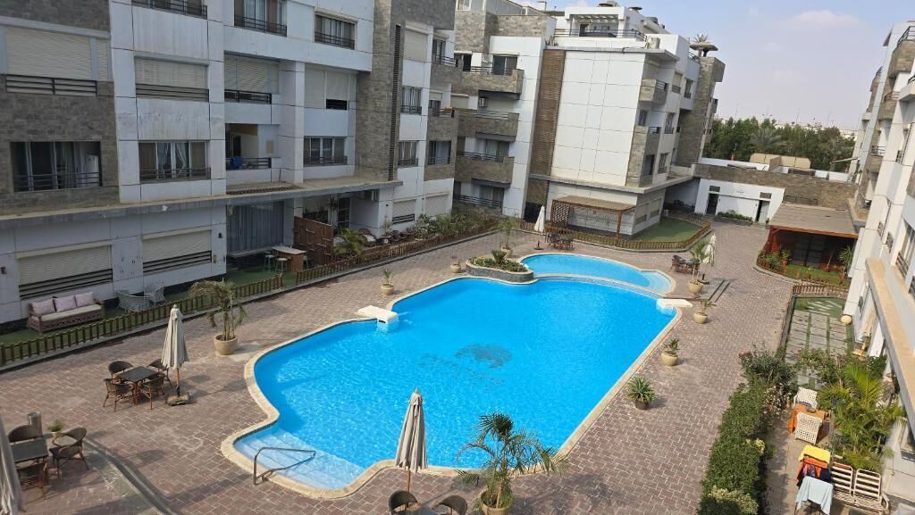 Un edificio residencial con piscina, mobiliario exterior y jardín.
