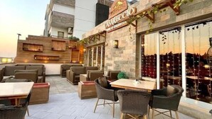 A rooftop patio area with outdoor seating, a stone facade building with a sign, and a clear sky. - Maison 7 New Cairo  (New Cairo)