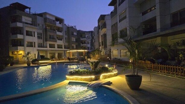 A swimming pool surrounded by multi-story buildings with balconies, outdoor seating, and potted plants. - Maison 7 New Cairo  (New Cairo)
