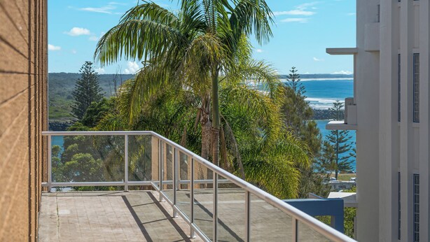 A balcony with a view of the ocean and palm trees.