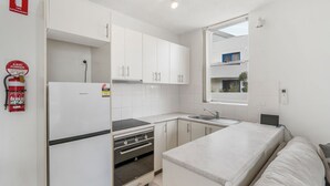 A compact kitchen with white cabinets, a built-in oven, a sink, and a window overlooking a balcony.