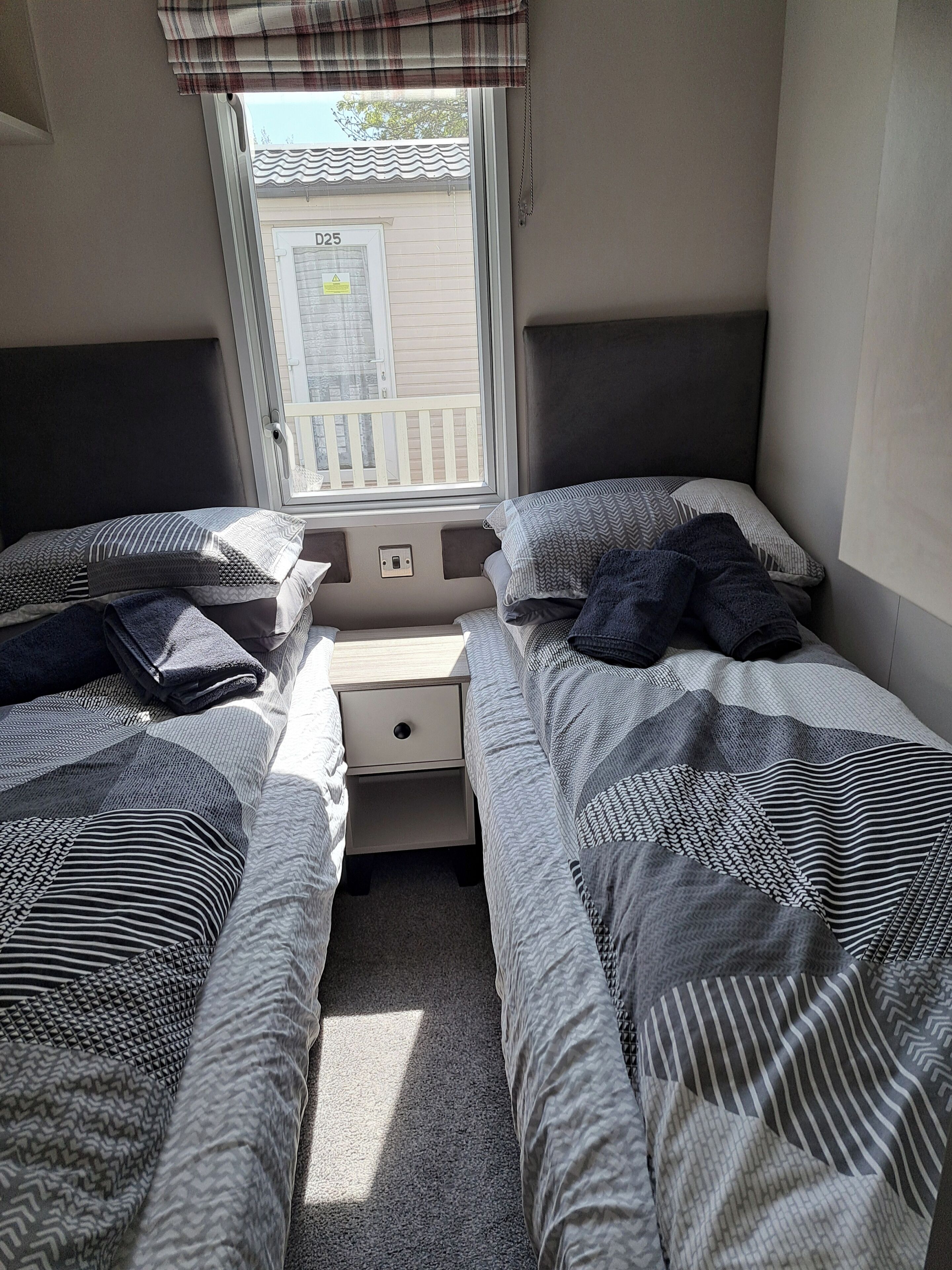 A small, compact room with two beds, a nightstand, and a window with a view of a building outside.