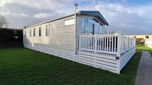 A mobile home with a fenced deck, a small porch, and a clear sky.