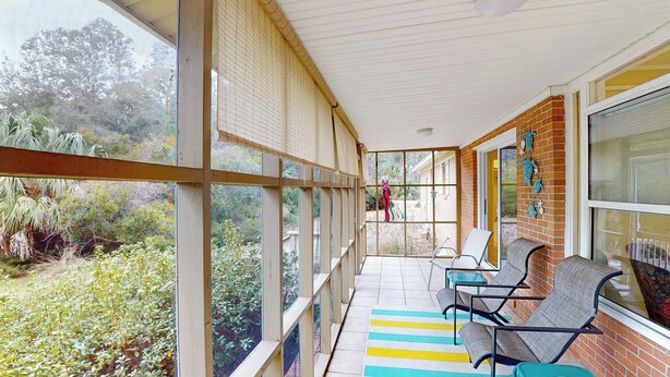 A covered porch with a view of a garden, a brick wall, and a seating area with chairs and a table.