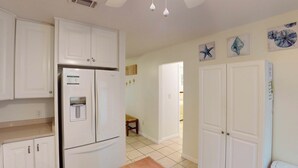 A kitchen with white cabinets, a refrigerator, and a water dispenser. There are three wall-mounted artworks depicting sea creatures.