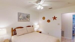 A bedroom with a bed, a nightstand, a ceiling fan, a painting, and wall decorations.