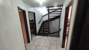 A hallway with a wooden staircase leading to a second floor. The floor is tiled with a marble-like pattern. - House in the Central Beach of Guaratuba (Guaratuba)