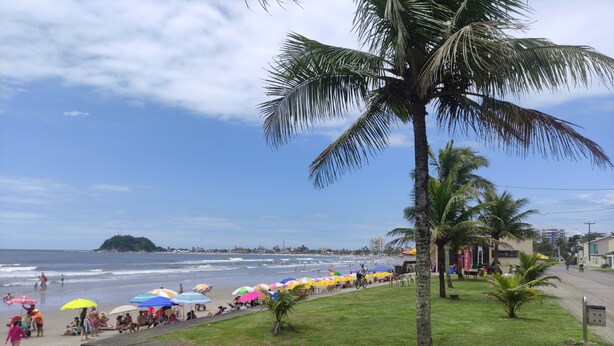 A beach with palm trees, umbrellas, and a cyclist. - House in the Central Beach of Guaratuba (Guaratuba)