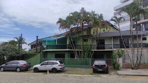 A two-story building with a green facade, a covered balcony, and a parking area with three cars. - House in the Central Beach of Guaratuba (Guaratuba)