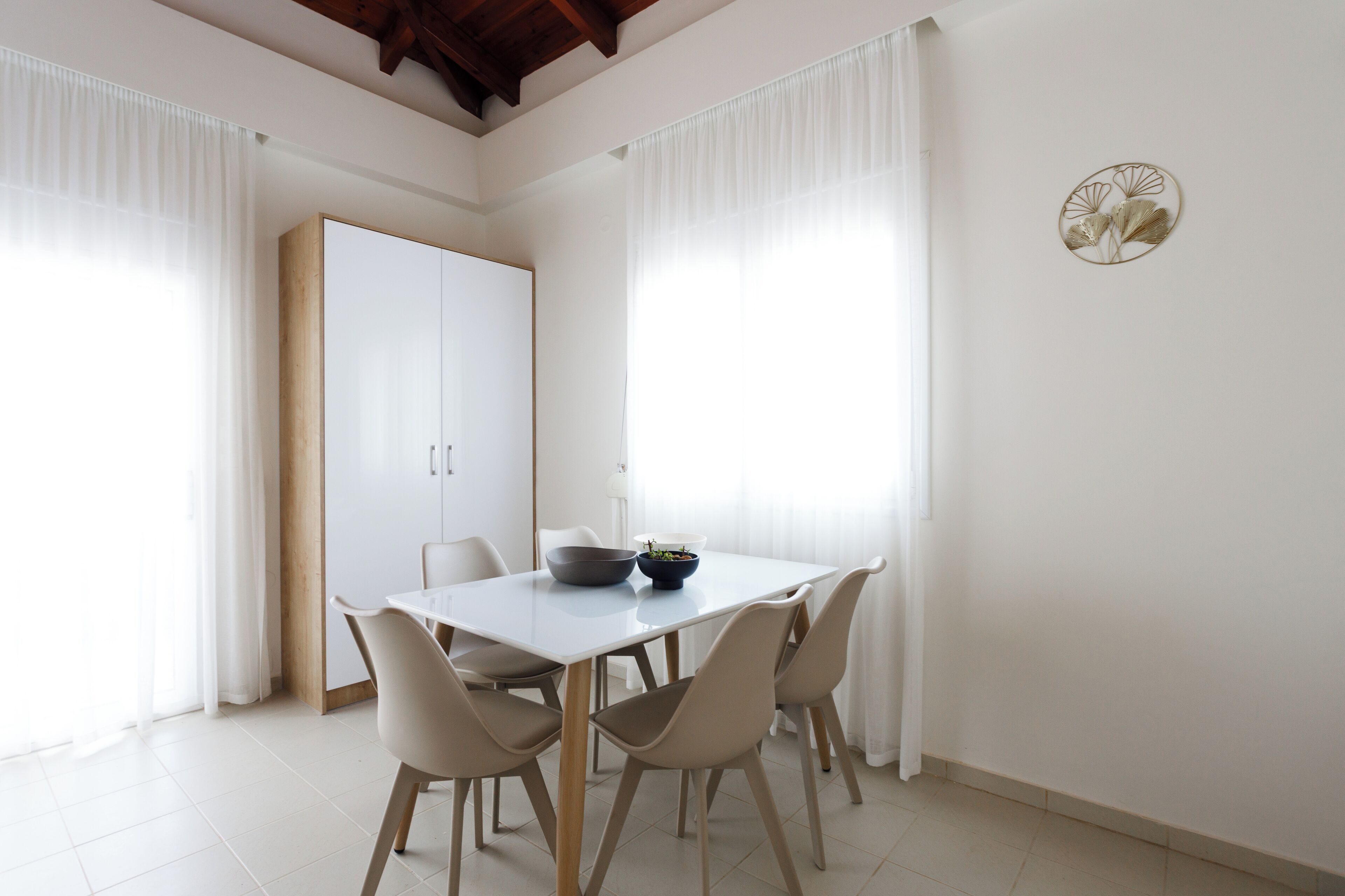 Uma área de refeições com uma mesa branca, cadeiras bege e uma tigela de frutas.