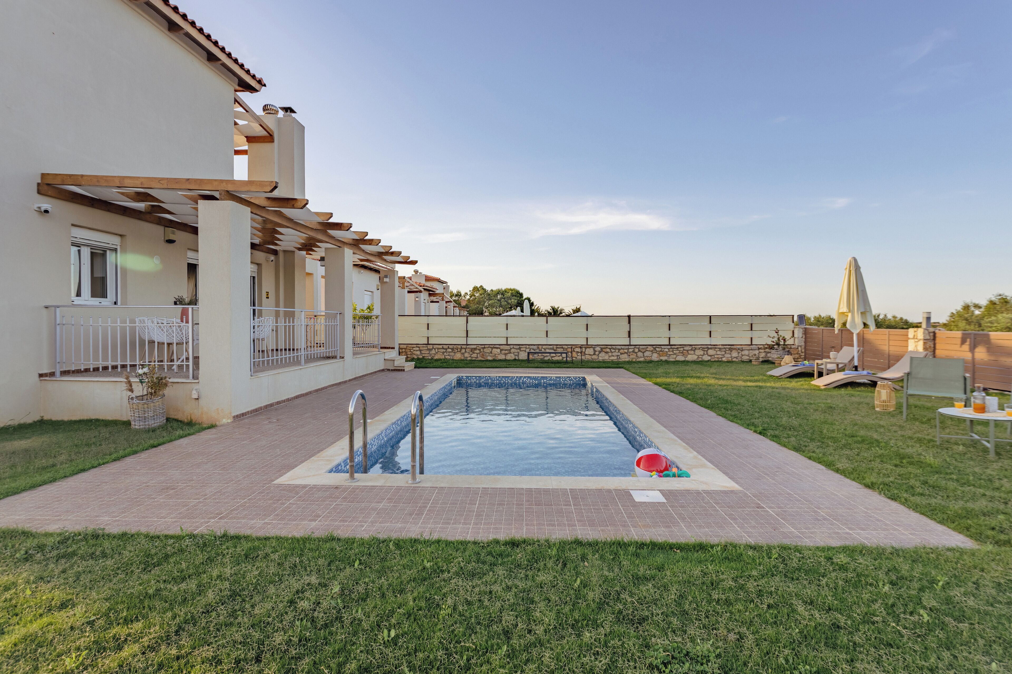 A swimming pool with a pergola, a covered patio, and a stone wall.