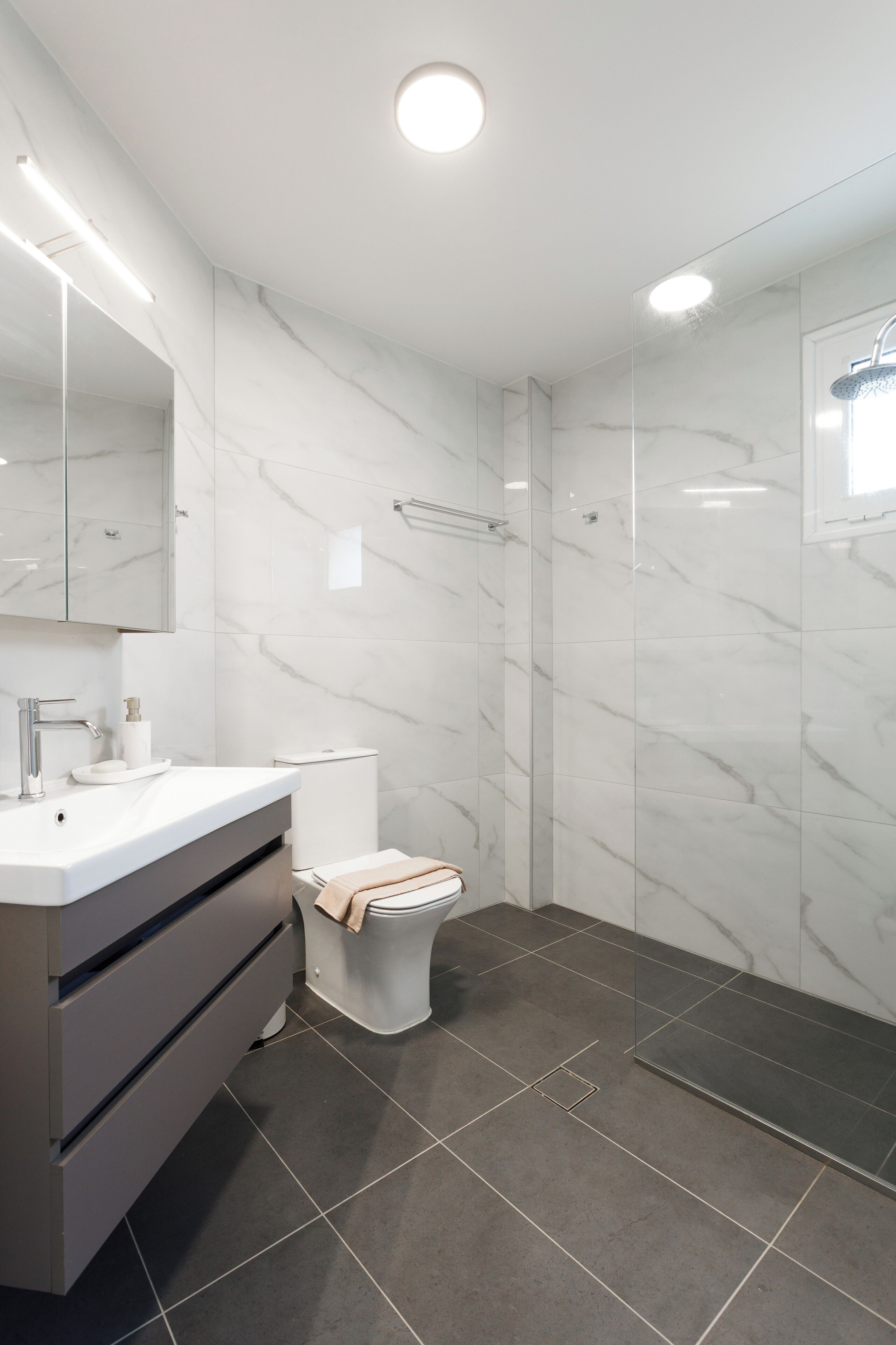 Un bagno moderno con una parete in marmo bianco, un lavabo grigio e cabina doccia in vetro.
